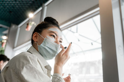 Low angle view of woman wearing mask applying face pack