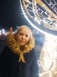 Portrait of woman standing against illuminated light at night