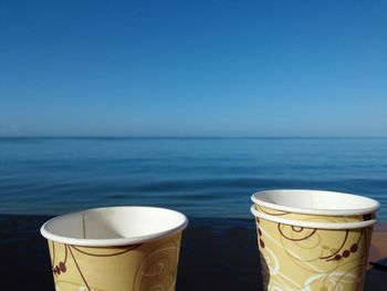 Coffee cup by sea against clear sky