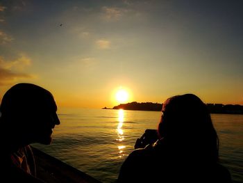 Rear view of silhouette couple sitting on sea during sunset