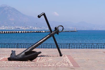 Statue of anchor by river with jetty