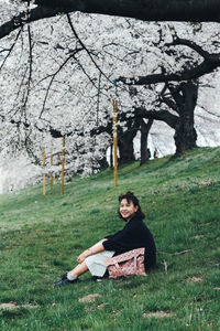 Portrait of woman sitting on field against cherry blossom trees