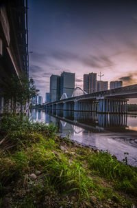 Bridge over river by buildings against sky during sunset