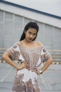 Portrait of young woman with hands on hip standing in city