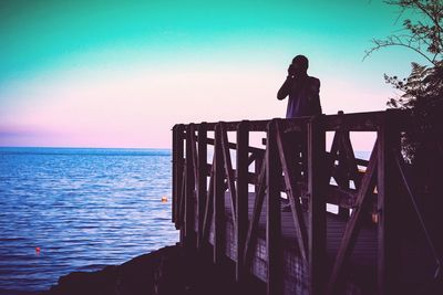 Silhouette person standing on railing against sea