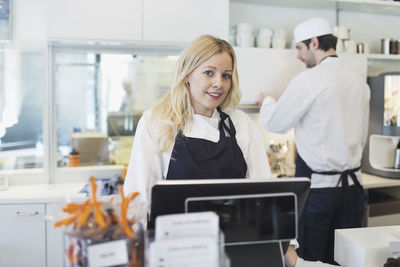 Portrait of confident female owner standing at checkout counter in cafe