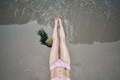 A young girl in a bikini lying on the sand on the beach with a pineapple. vacation concept