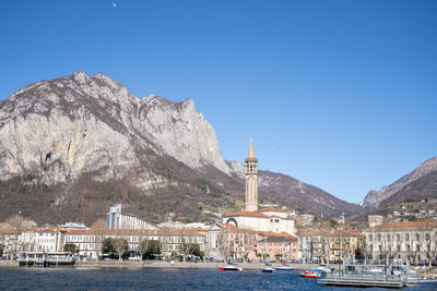 Buildings by sea against clear blue sky