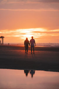 Silhouette people walking at beach during sunset