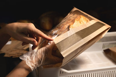 Women's caring hands pack fresh artisan bread in a paper bag with a transparent insert.