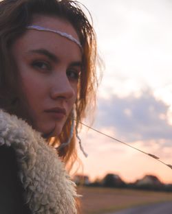 Close-up portrait of young woman looking away against sky during sunset