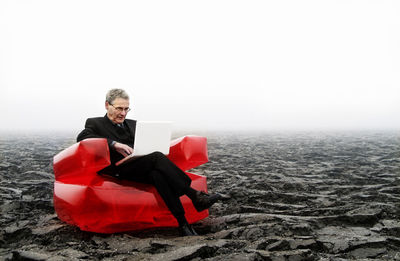 Businessman using laptop while sitting on landscape against sky