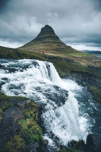 Scenic view of waterfall by mountain against sky