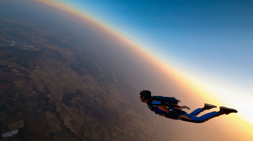 High angle view of men flying over the earth during sunset skydiving jump.