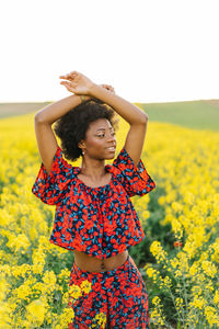 Portrait of beautiful young woman standing by yellow flower on field