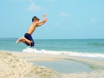 Full length of shirtless man jumping on beach against sky
