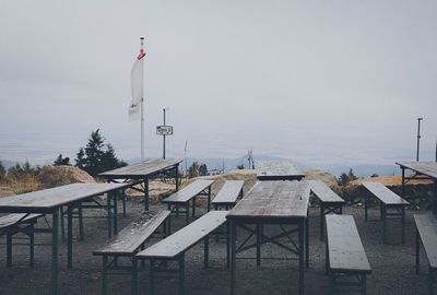 Empty chairs and tables against sky during winter