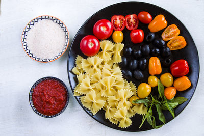 Pasta ingredients, raw pasta, cherry tomatoes, olives and basil leaves on the black plate