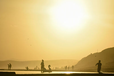 Silhouette people on beach against sky during sunset