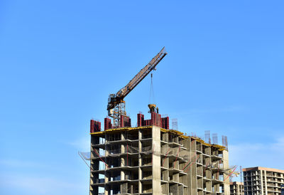 Low angle view of crane by building against clear blue sky