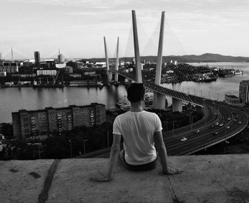 Rear view of man sitting on bridge over river