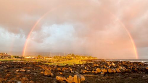 Panoramic view of rainbow over rocks against sky during sunset