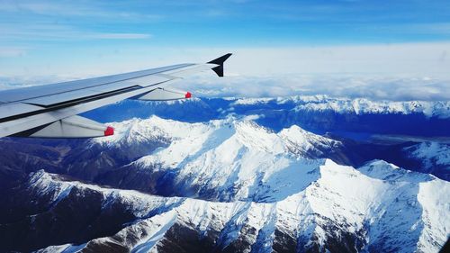 Cropped image of airplane flying over snowcapped mountains against sky