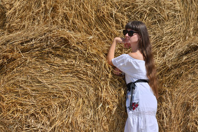 Mid adult woman standing against stacked hay bales on agricultural field