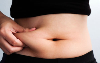 Midsection of woman touching stomach against white background