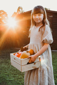 A girl in the evening sun stands in the backyard of a house with a box of pumpkins. harvesting. 