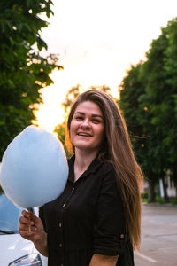 Portrait of smiling young woman standing against trees