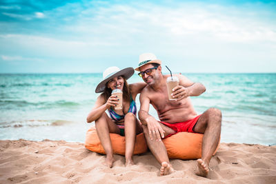 Mature couple having drinks while sitting at beach