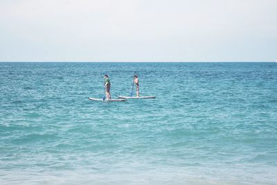 Men surfing in sea against sky