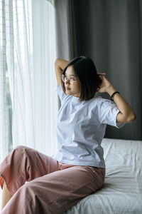 Young woman looking away while sitting on bed at home