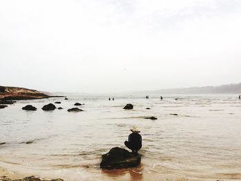 Rear view of man sitting on beach against clear sky