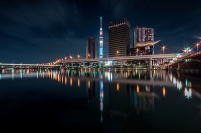 Illuminated buildings by lake against sky in city at night