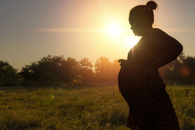 Pregnant woman standing in the meadow warm tones.