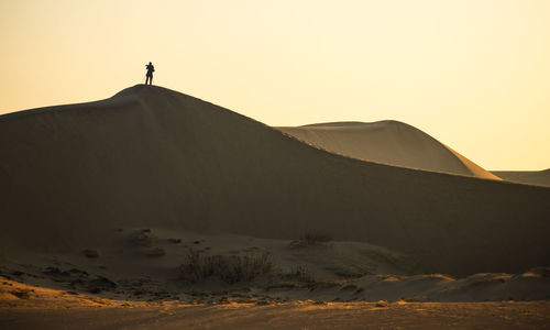 Silhouette person on arid landscape against clear sky during sunset