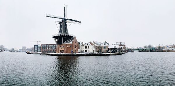 Houses by river against sky during winter