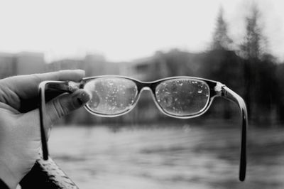 Close-up of hand holding sunglasses against sky