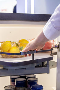 Human hand pushes modern pull-out shelf with some fruits  in a kitchen cupboard