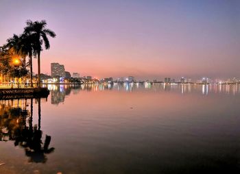 Illuminated buildings by sea against sky at night