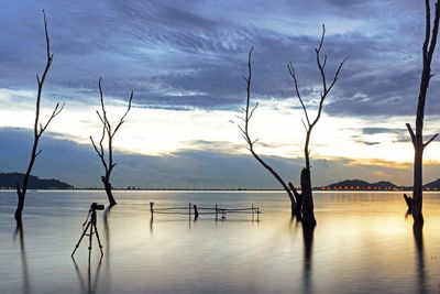 Silhouette wooden posts in sea against sky at sunset