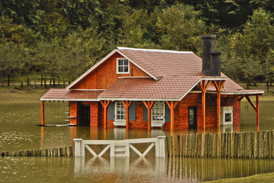 Exterior of house by lake and trees against sky