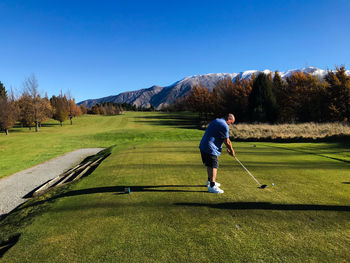 Rear view of man teeing off against clear blue sky