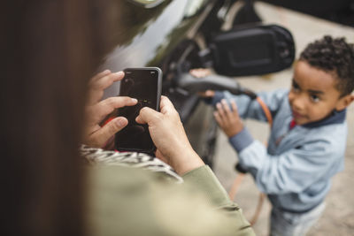 High angle view of boy charging electric car while looking at mother using smart phone