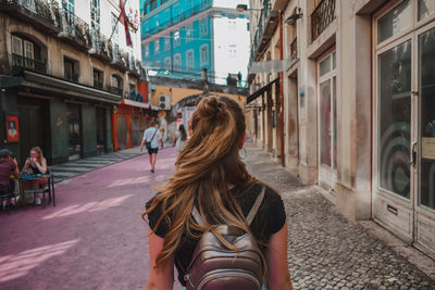 Rear view of woman walking on street amidst buildings in city