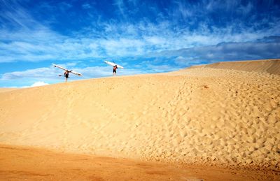 Men holding surf ski walking on shore at beach against sky