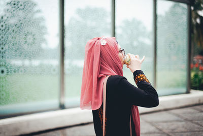 Side view of woman standing against window