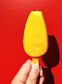 Cropped hand holding ice cream cone against yellow background